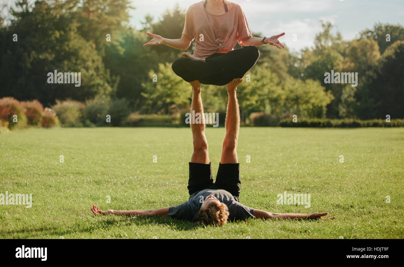 Strong young couple doing acroyoga outdoors. Man and woman in park practising pair yoga poses. Stock Photo