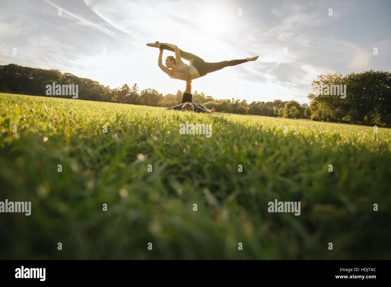 Fit young couple doing acroyoga on grass. Man and woman in park practising pair yoga poses. Stock Photo