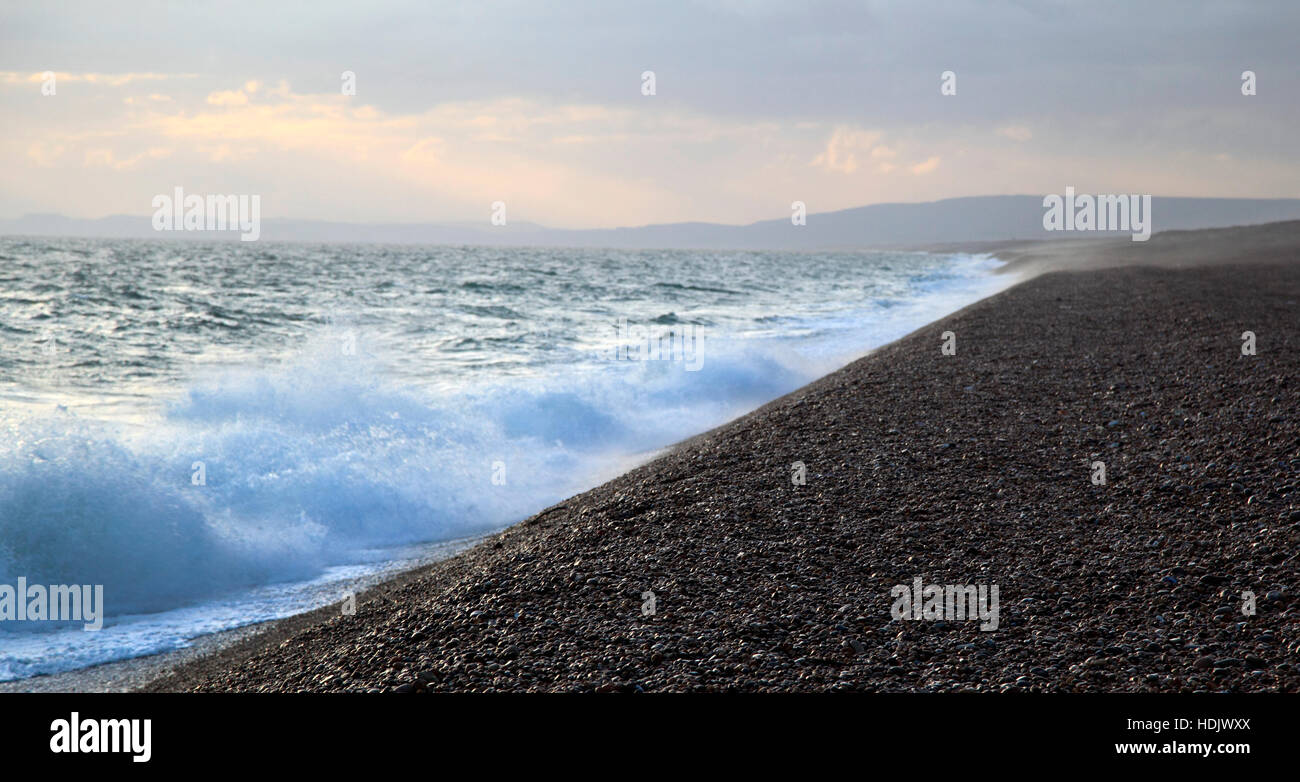 Waves crash onto Chesil Beach, part of the Jurassic Coast as dusk