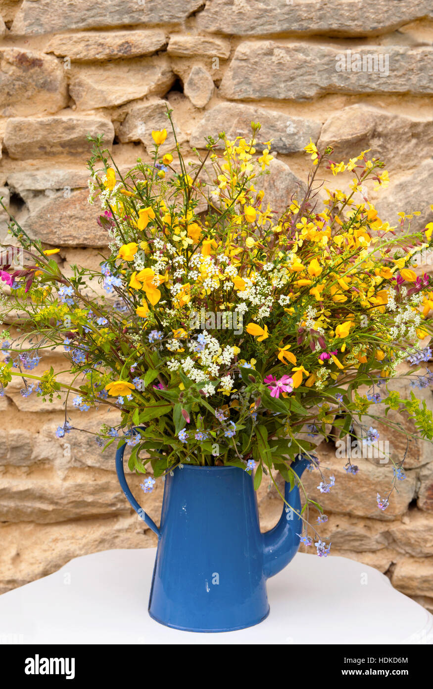 Bouquet field flowers in blue watering can in front of a stone