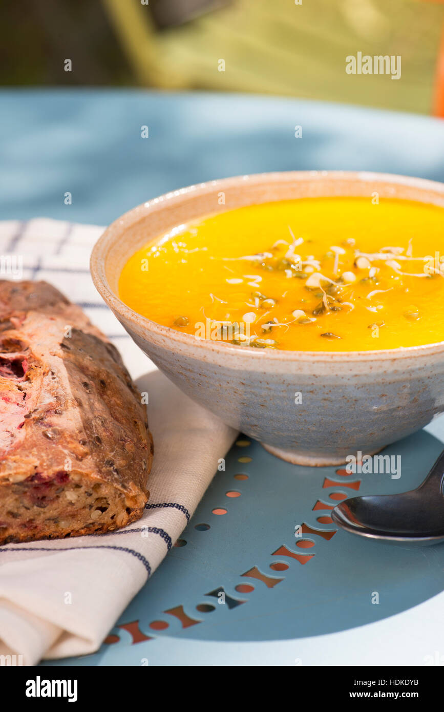 Bowl of hot carrot and ginger soup served with freshly baked bread. Colorful food. Stock Photo
