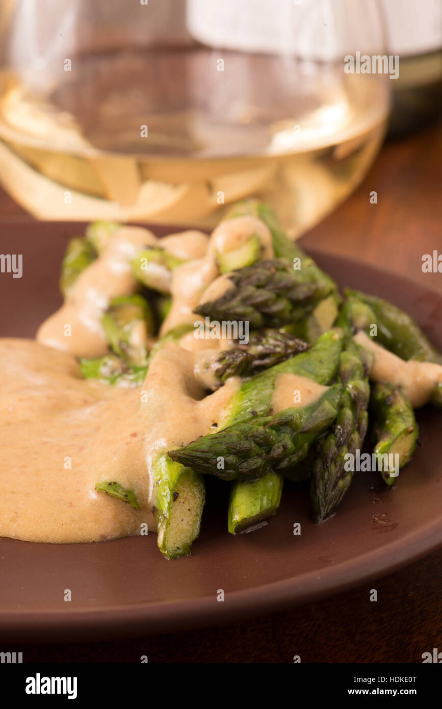Fried green asparagus and sauce. Glass of white wine in the background. Stock Photo