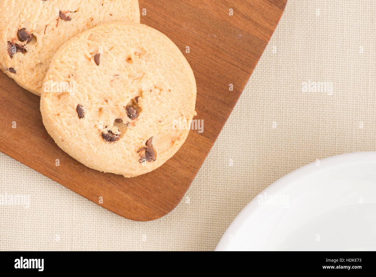 Chocolate chip cookies on wooden cutting board from above in close up. Sweet food, dessert or snack. The cookies are served on a kitchen table. Stock Photo
