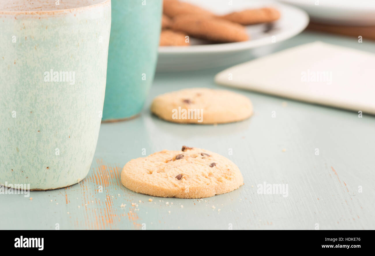 Chocolate chip cookies and coffee or tea mugs. Sweet food, dessert or snack. The cookies are served on a kitchen table. Stock Photo