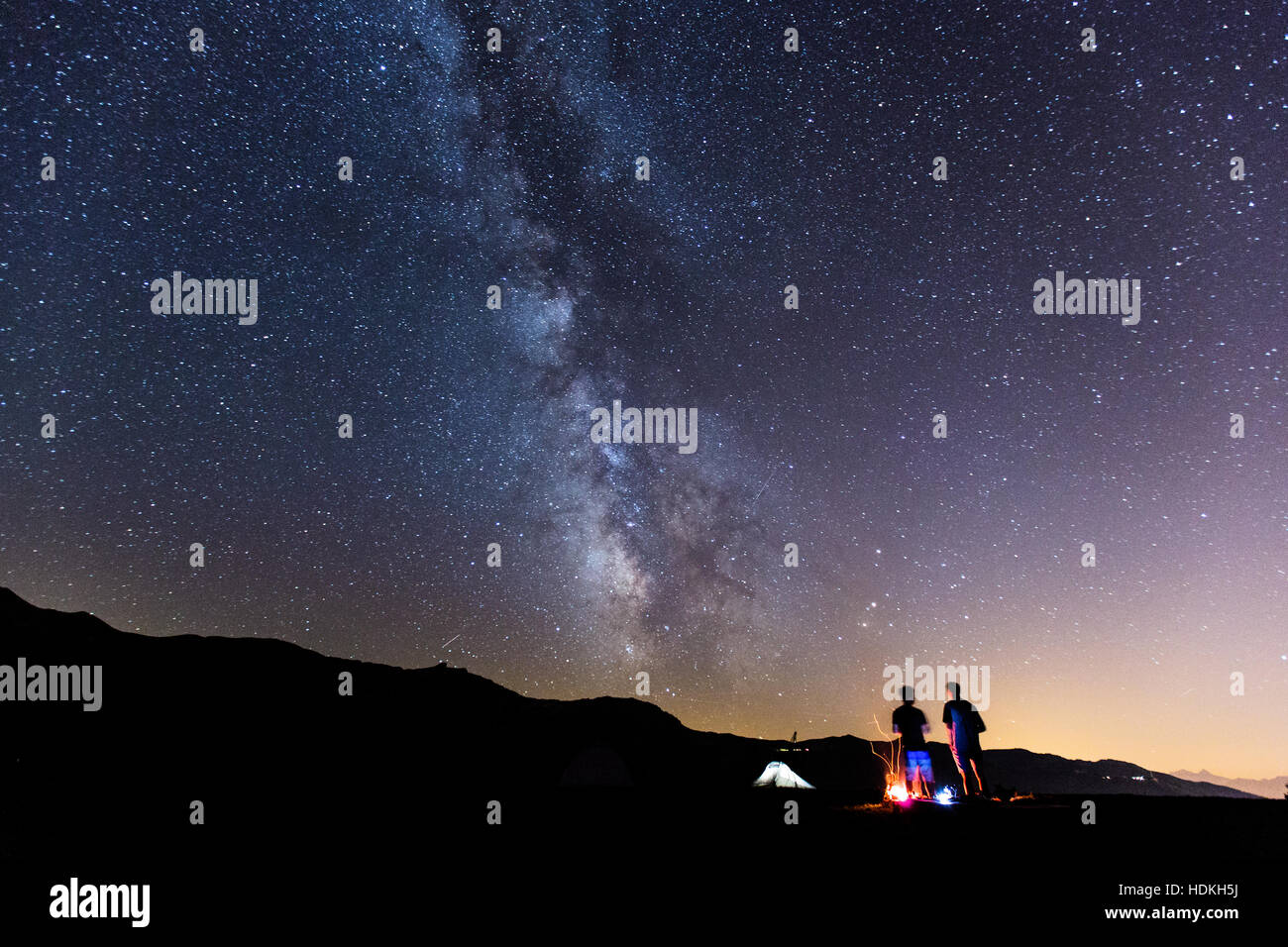 Milky Way. Night sky with stars and silhouette of two man around a fire Stock Photo