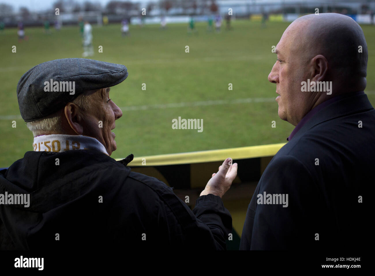 Two home supporters chatting during the first-half at the Delta Taxis Stadium, Bootle, Merseyside as City of Liverpool hosted Holker Old Boys in a North West Counties League division one match. Founded in 2015, and aiming to be the premier non-League club in Liverpool, City were admitted to the League at the start of the 2016-17 season and were using Bootle FC's ground for home matches. A 6-1 victory over their visitors took 'the Purps' to the top of the division, in a match watched by 483 spectators. Stock Photo