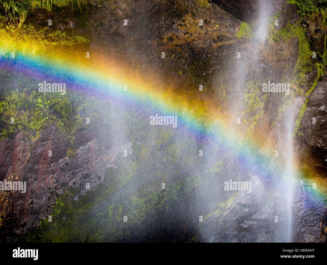 Rainbow caused by refraction of sunlight in the fine mist of a waterfall in Milford Sound in Fjordland South Island New Zealand Stock Photo