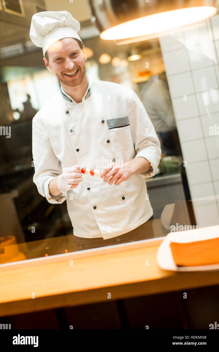 Young chef with white uniform standing at a modern kitchen in the restaurant and preparing food Stock Photo