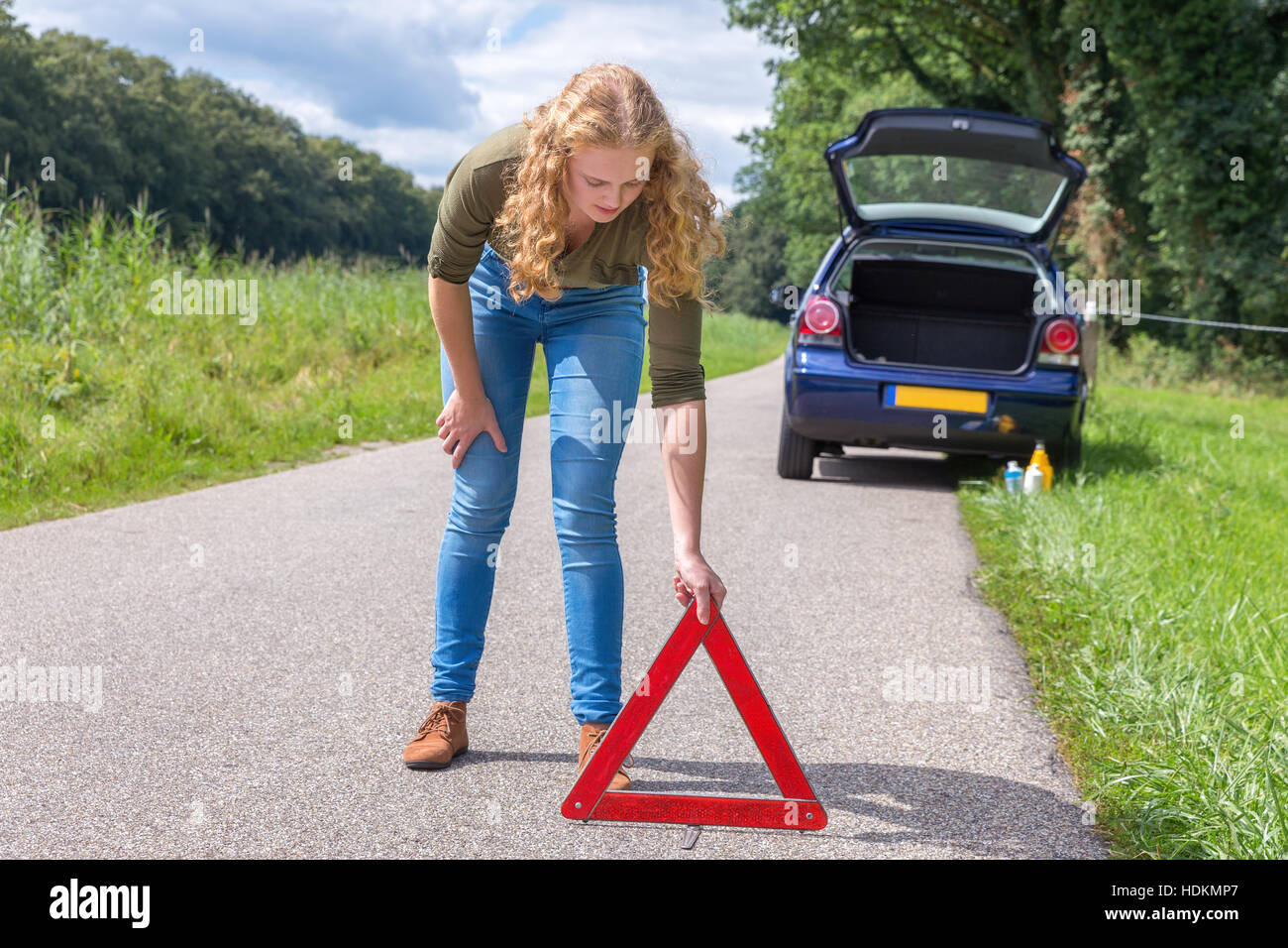 European teenage girl placing hazard warning triangle on country road Stock Photo