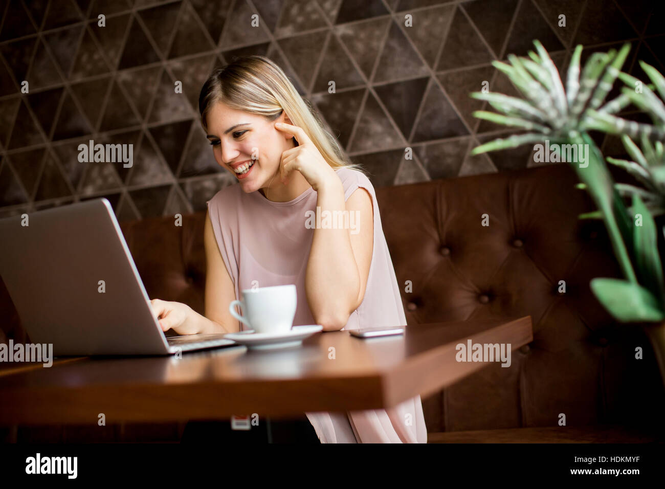Freelance young woman sitting in the cafeteria with laptop and drinking coffee Stock Photo