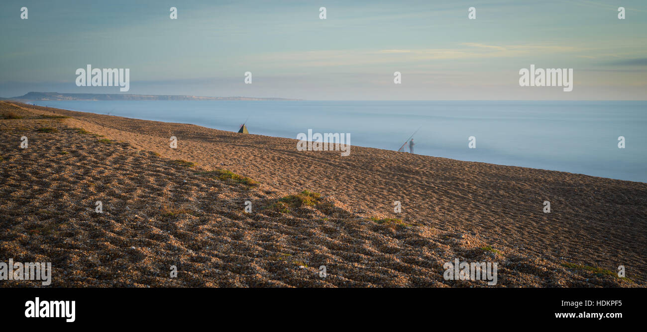 Looking west along Chesil beach from the Isle of Portland on a sunny day  with an onshore wind that has created some surf. Some anglers can be seen  fis Stock Photo 