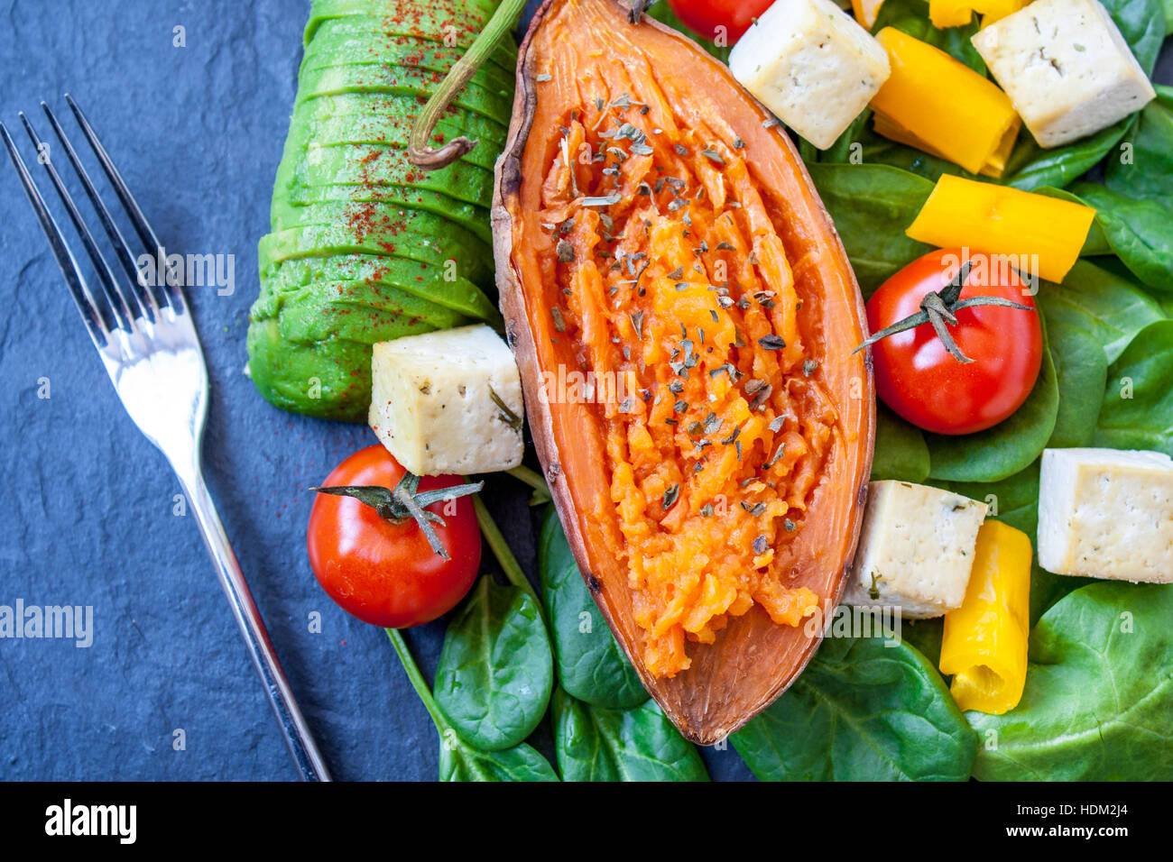 Salad with grilled vegetables: grilled sweet potatoes, tomatoes, avocados, spinach, tofu and pepper on dark slate background. Perfect for the detox di Stock Photo