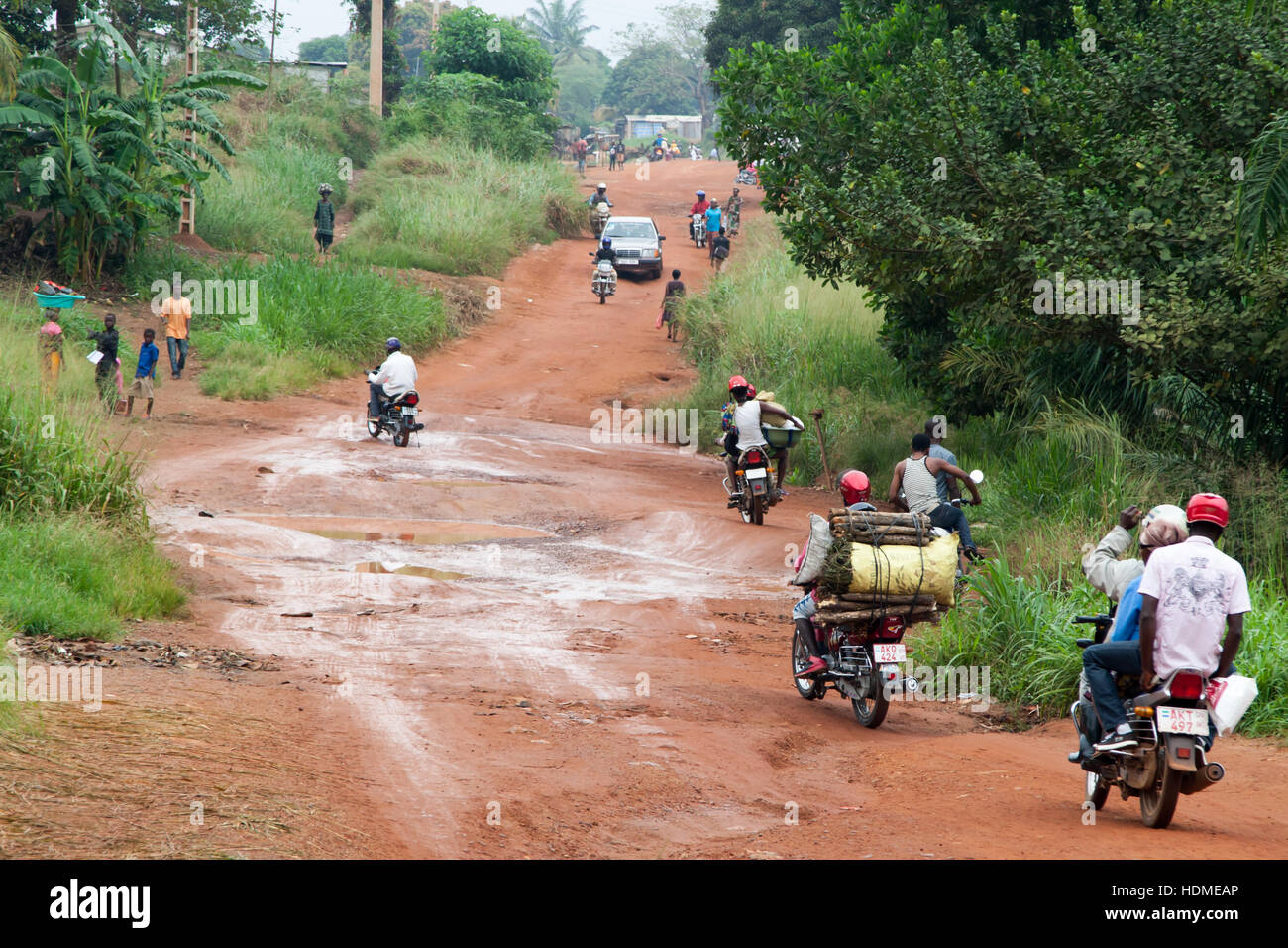 Muddy Gravel Road in Sierra Leone populated by pedestrians, motorcycles and one car. Main highway near Kenema in Sierra Leone Stock Photo
