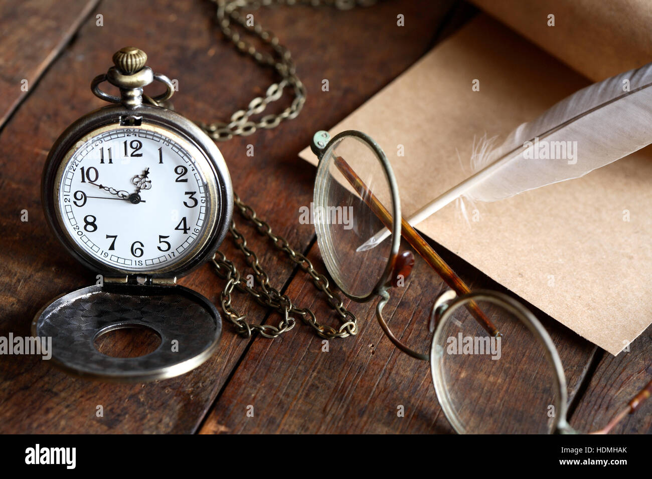Old spectacles near watch and feather on nice old wooden background Stock Photo