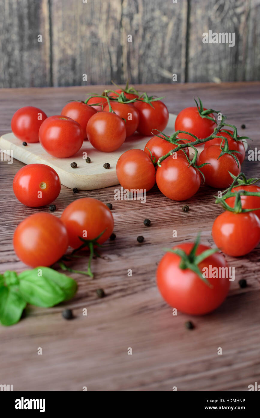 Scattered cherry tomatoes with pepper and leaves of basil on the wooden ...