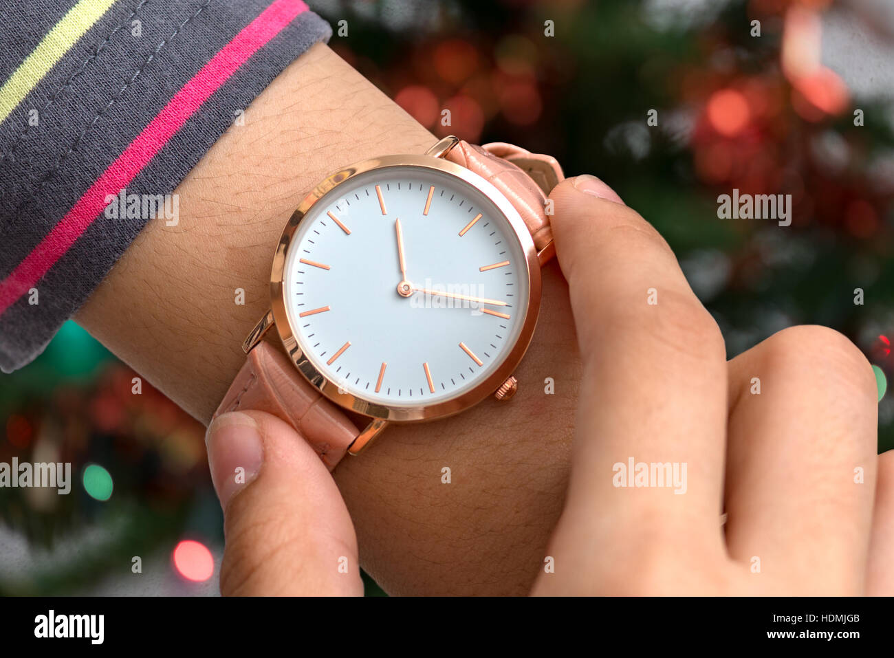 Girl's hand with wrist watch in Christmas time in front of Christmas tree in background Stock Photo