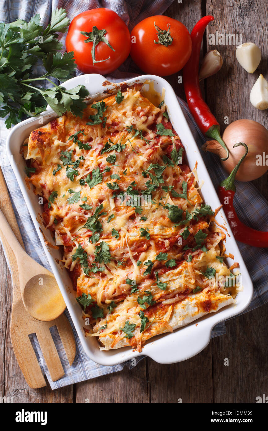 Mexican enchilada in a baking dish with the ingredients on the table. vertical view from above close-up Stock Photo