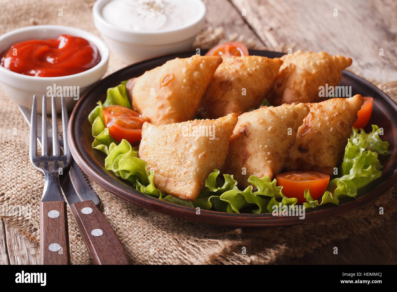 Indian samosa delicious pastry on a plate with tomatoes and lettuce on a wooden table. horizontal Stock Photo