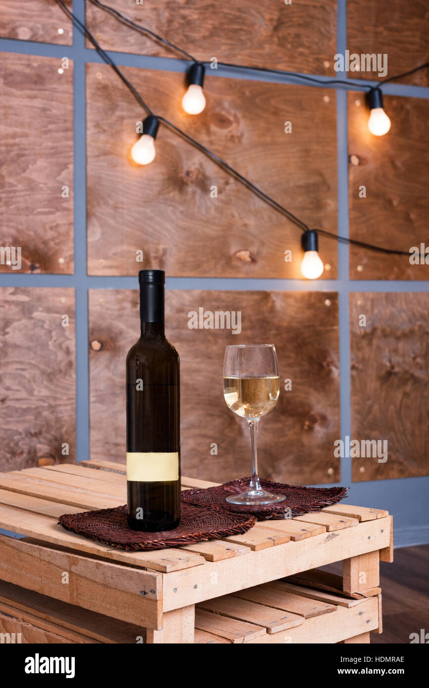 Glass of white wine and bottle in modern loft interior with light ...