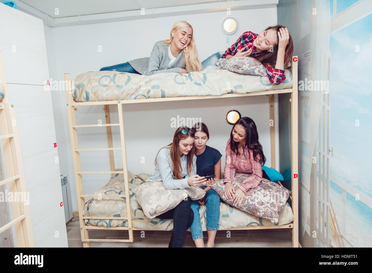 Beautiful girls sitting on a bed in hostel talk and have fun. 