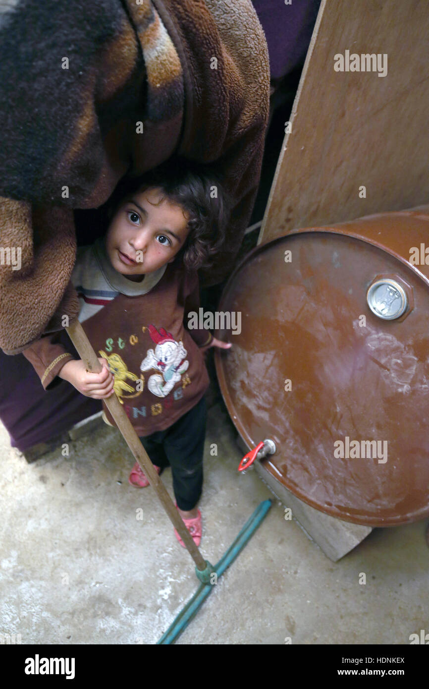 Syrian refugee child hides alongside a water barrel in the camp in the Bekaa Valley, Lebanon, close to the Syrian border. Stock Photo