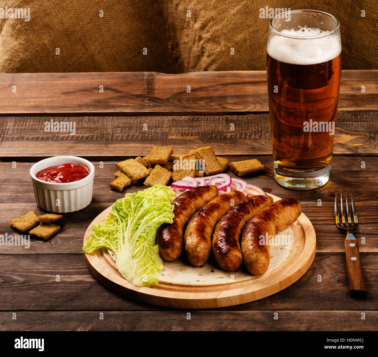 Grilled sausages with glass of beer, croutons and chinese cabbage on wooden table Stock Photo