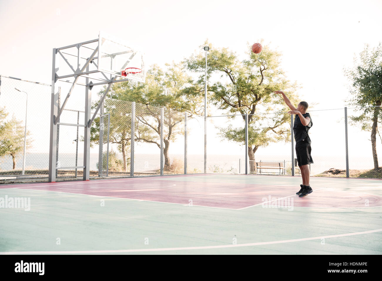 Picture of young basketball player practicing in the street with trees on background Stock Photo