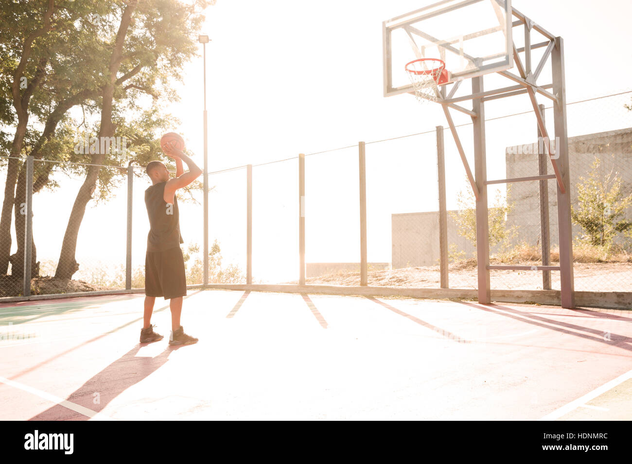 Picture of african basketball player practicing in the street with basketball hoop. Looking at hoop. Stock Photo
