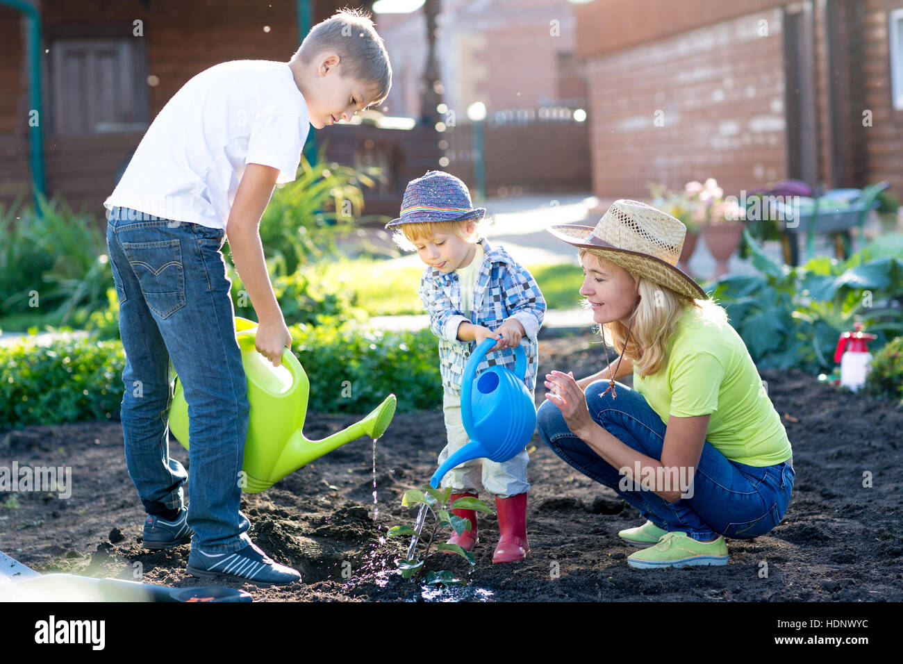 Mother with two children sons planting a tree and watering it together in garden Stock Photo