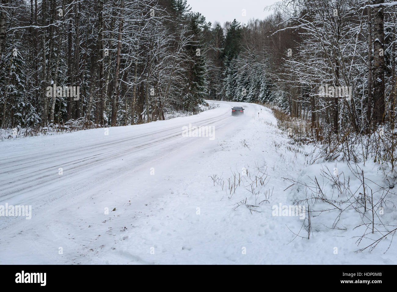 car traveling on a snowy forest road between the trees Stock Photo