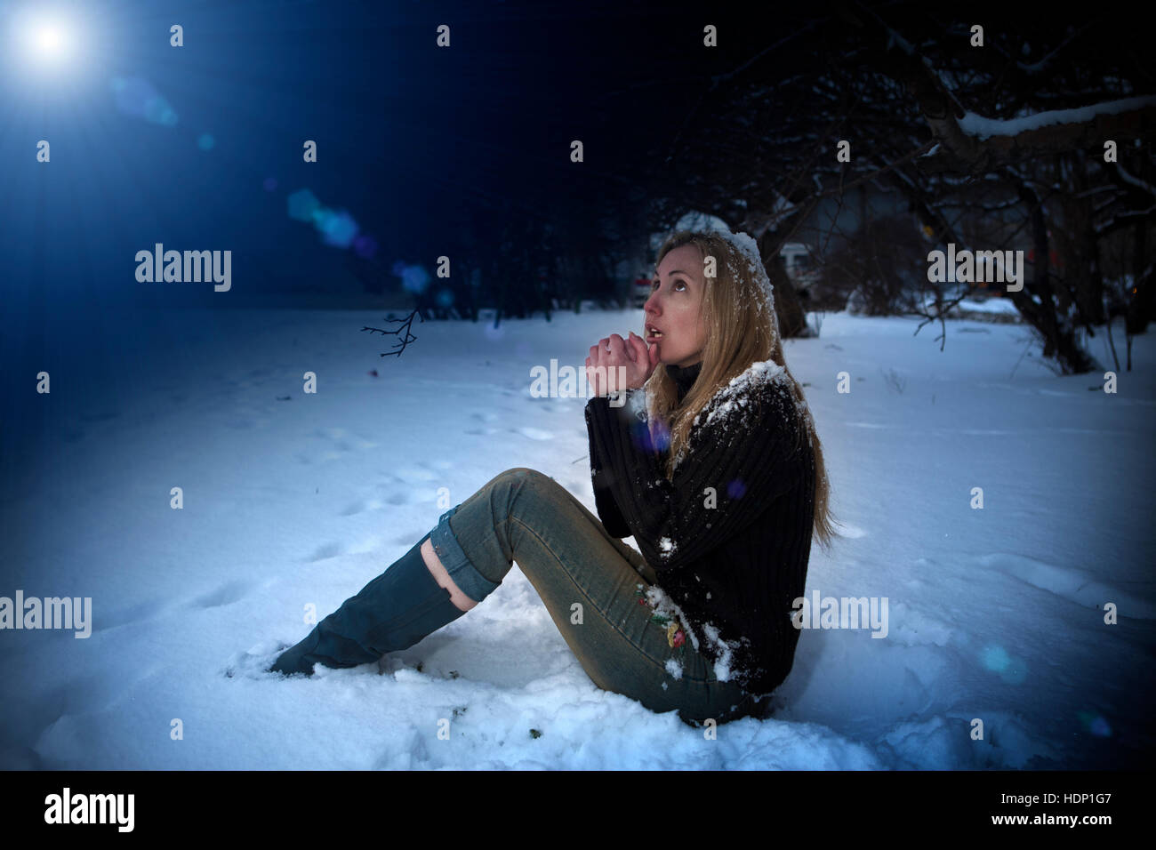 The young beautiful frozen woman sits in snow in the night park Stock