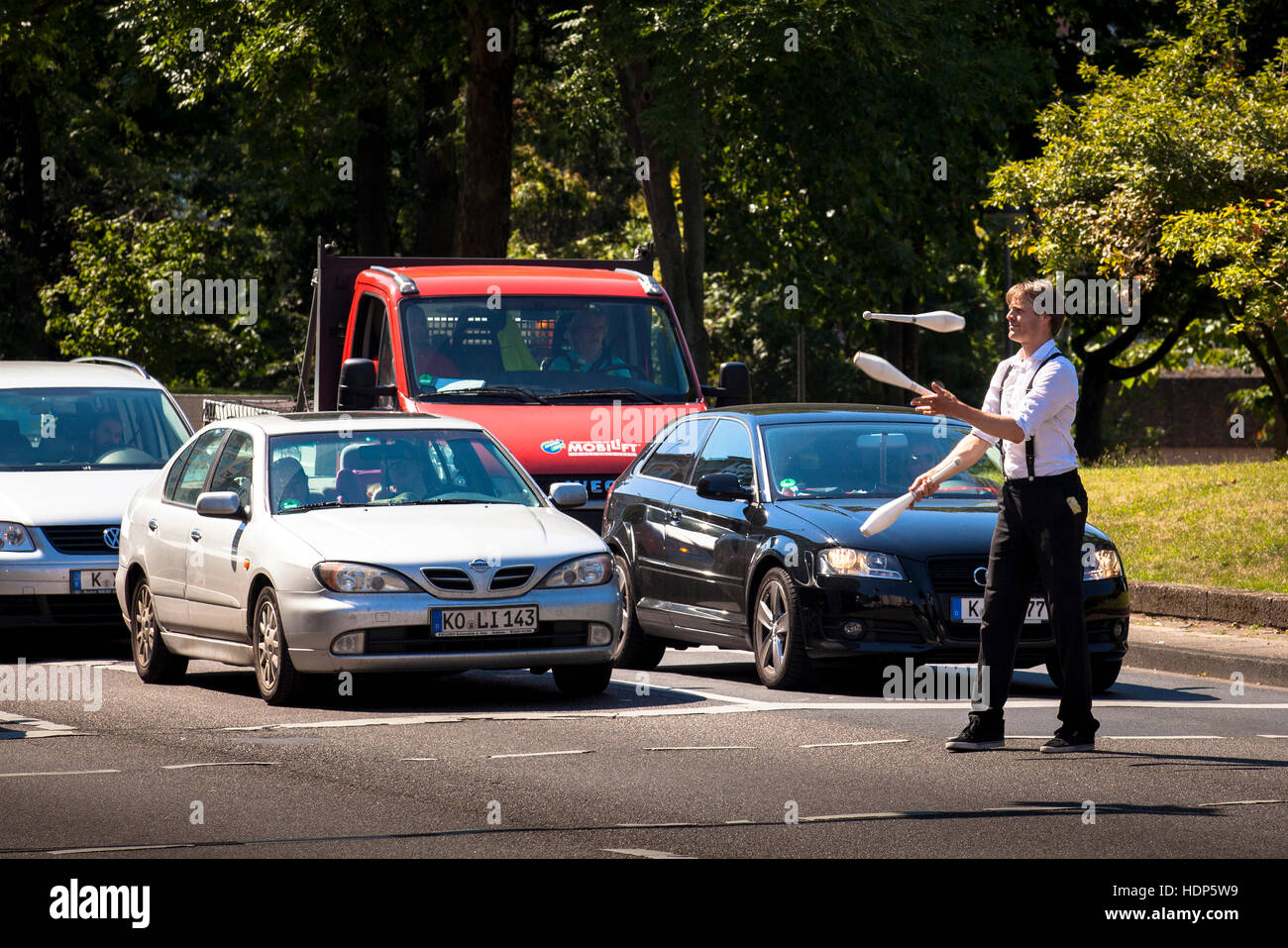 Germany,  Cologne, juggler in front of cars, waiting at traffic lights, after the performance he asks the drivers for a donation. Stock Photo