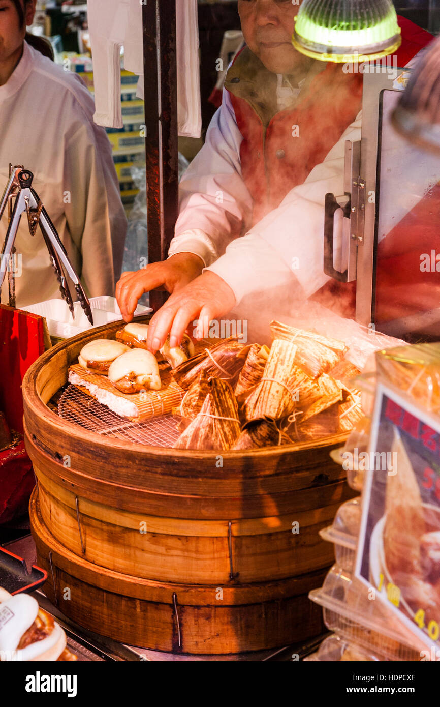 Japan, Kobe, Nankinmachi, Chinatown. Chinese food stall counter, Pork Belly buns being steamed in wooden container, with hand turning one. Stock Photo