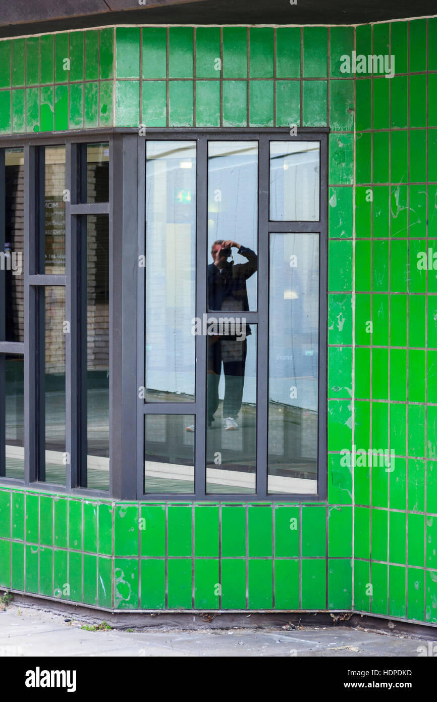Reflection in window of Archway library, surrounded by green tiles, of a person taking a photograph, London, UK Stock Photo