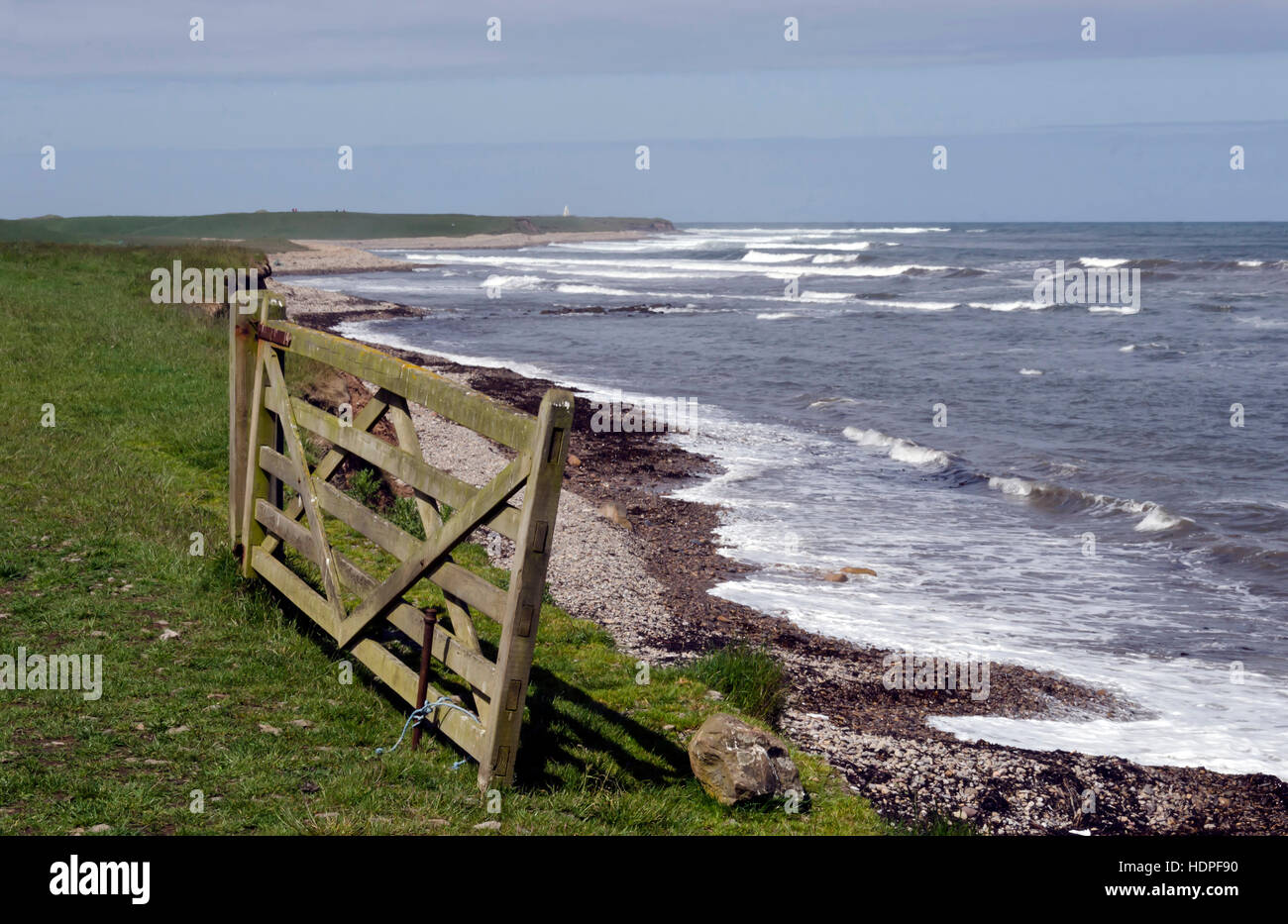 Rough sea off the coast of Lindisfarne (Holy Island) in Northumberland, England, with an old wooden gate in the foreground. Stock Photo