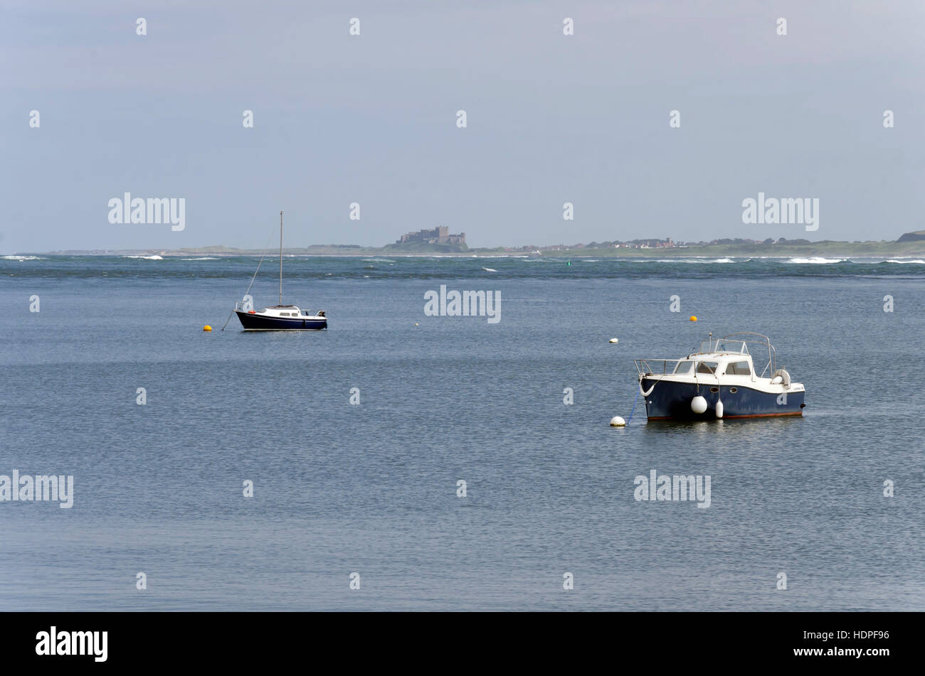 Small boats in the sea off Lindisfarne (Holy) Island in Northumberland, England with Bamburgh Castle in the distance. Stock Photo