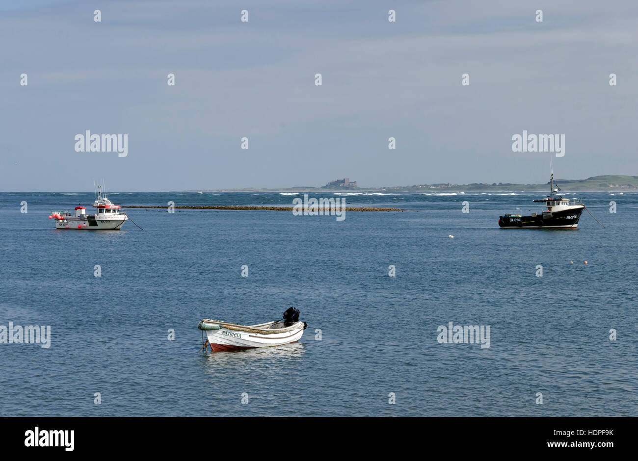 Small boats in the sea off Lindisfarne (Holy) Island in Northumberland, England with Bamburgh Castle in the distance. Stock Photo
