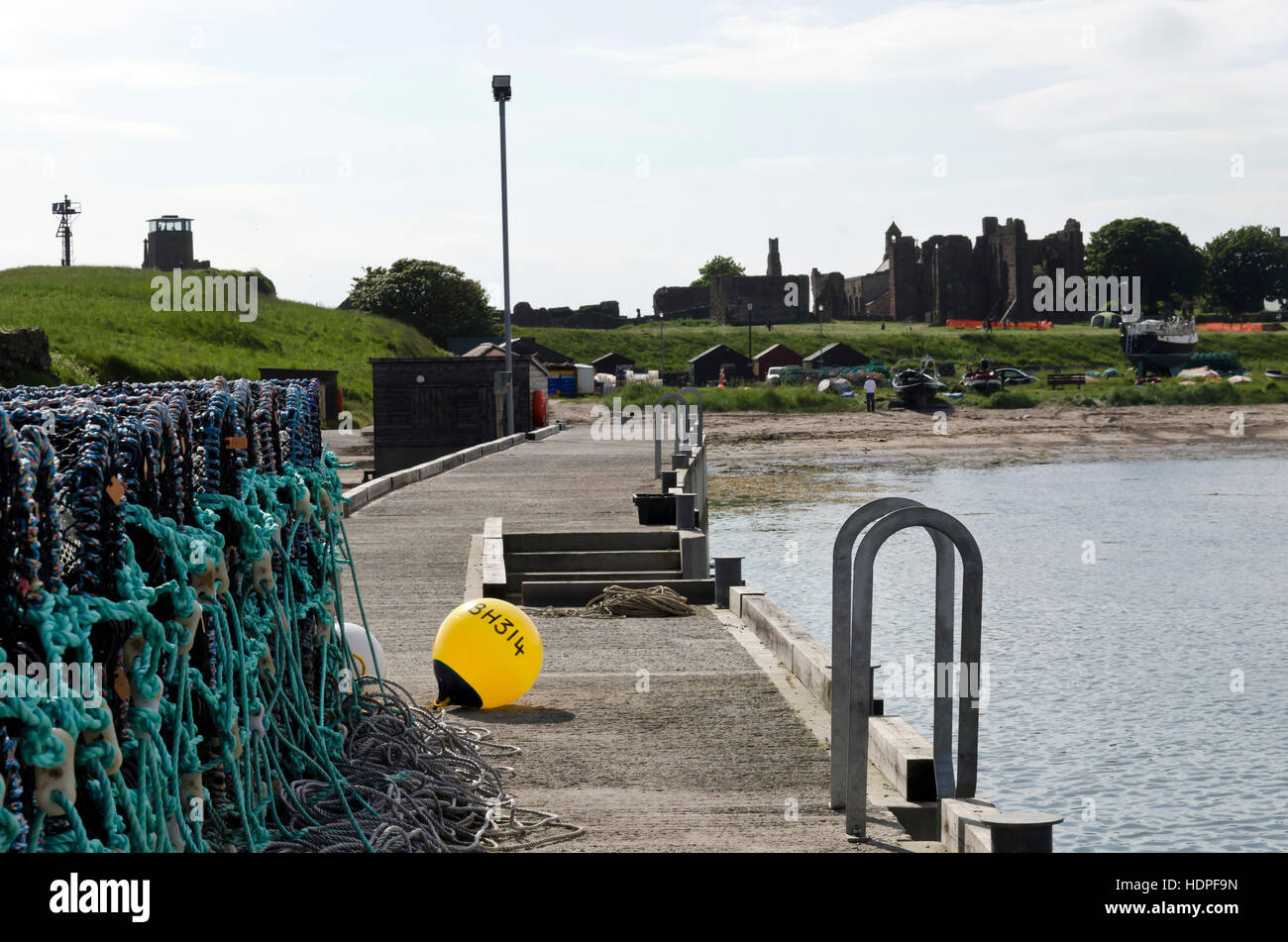 Lobster pots piled-up at the harbour at Lindisfarne (Holy) Island in Northumberland, England, with priory in the distance. Stock Photo