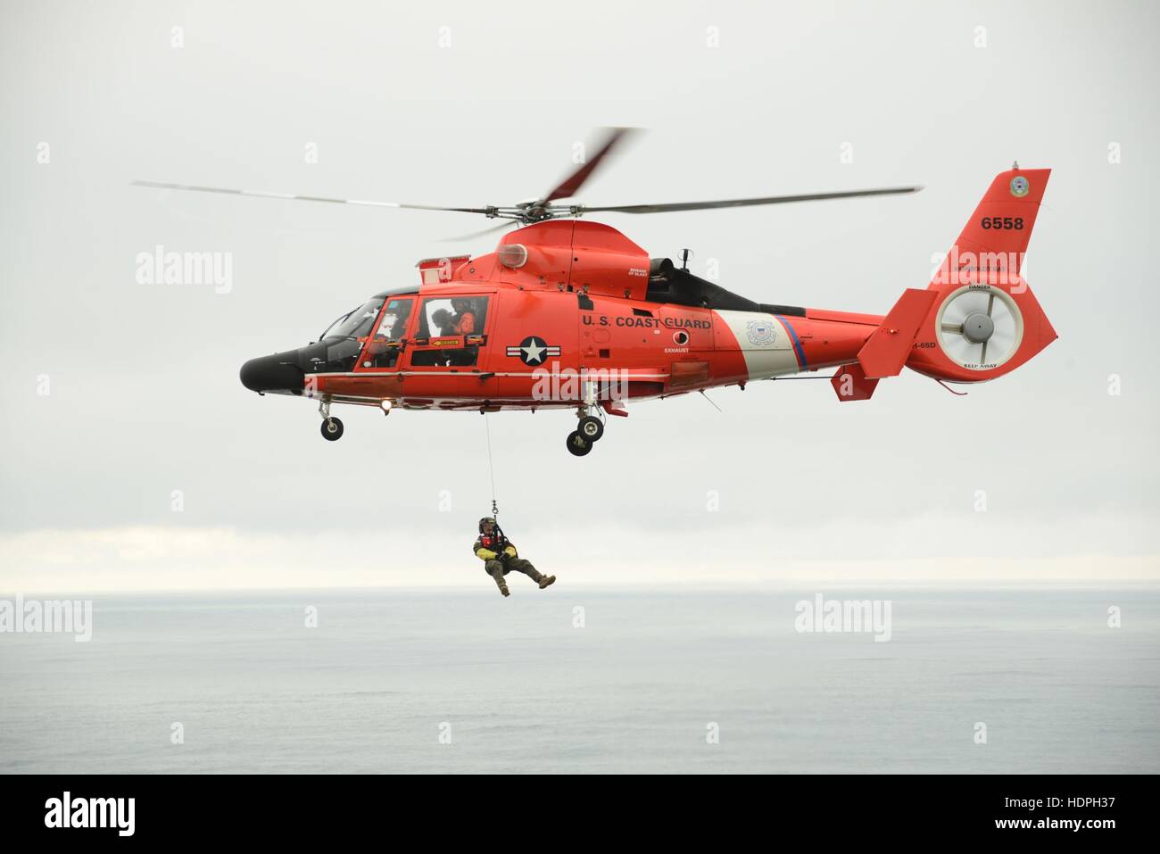 A U.S. Coast Guard pararescue officer dangles from a Eurocopter MH-65 Dolphin search and rescue helicopter during an Advanced Helicopter Rescue School training exercise near the North Head Lighthouse November 10, 2016 in Ilwaco, Washington. Stock Photo