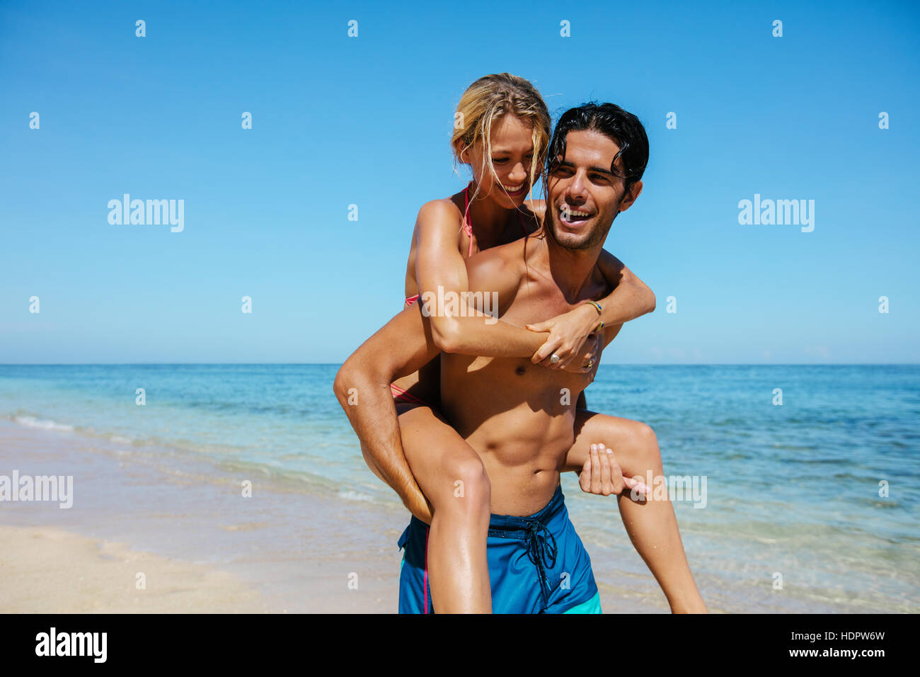 Portrait of man carrying girlfriend on his back. Couple enjoying piggyback ride on the beach vacation. Stock Photo