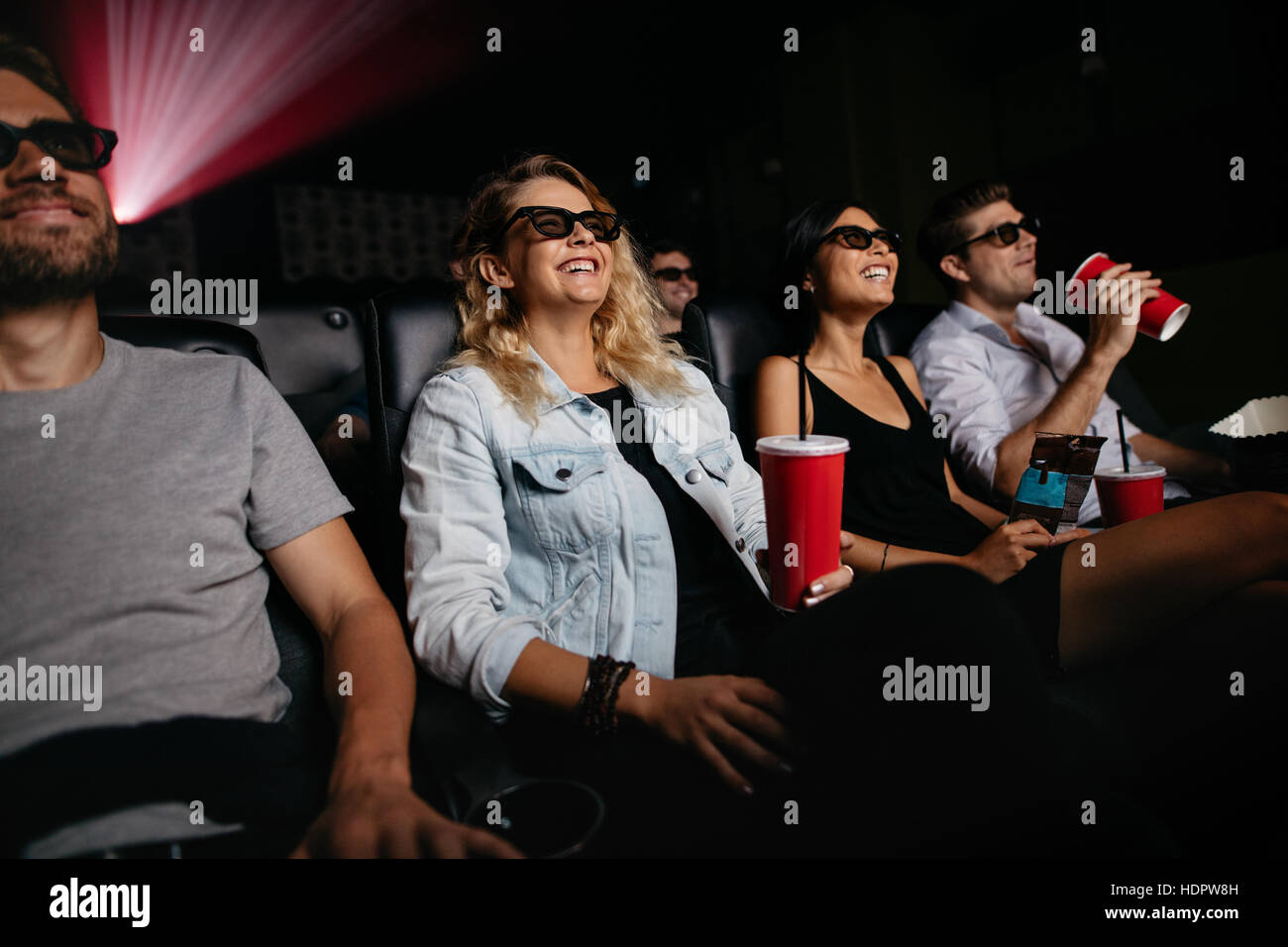Young women and men watching 3d movie in cinema. Group of people in theater with 3d glasses and drinks. Stock Photo