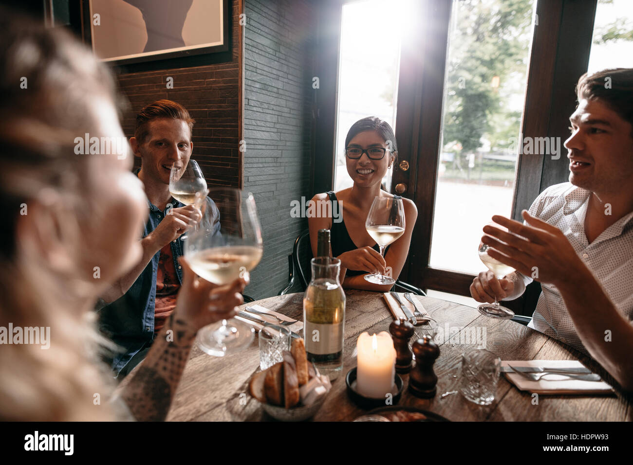 Indoor shot of young friends drinking wine at cafe. Group of men and women enjoying a glass of wine at restaurant. Stock Photo