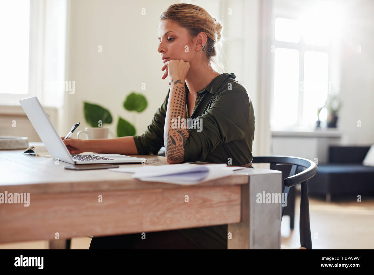 Side view shot of young woman working on laptop at home office. Caucasian female sitting at table using laptop. Stock Photo