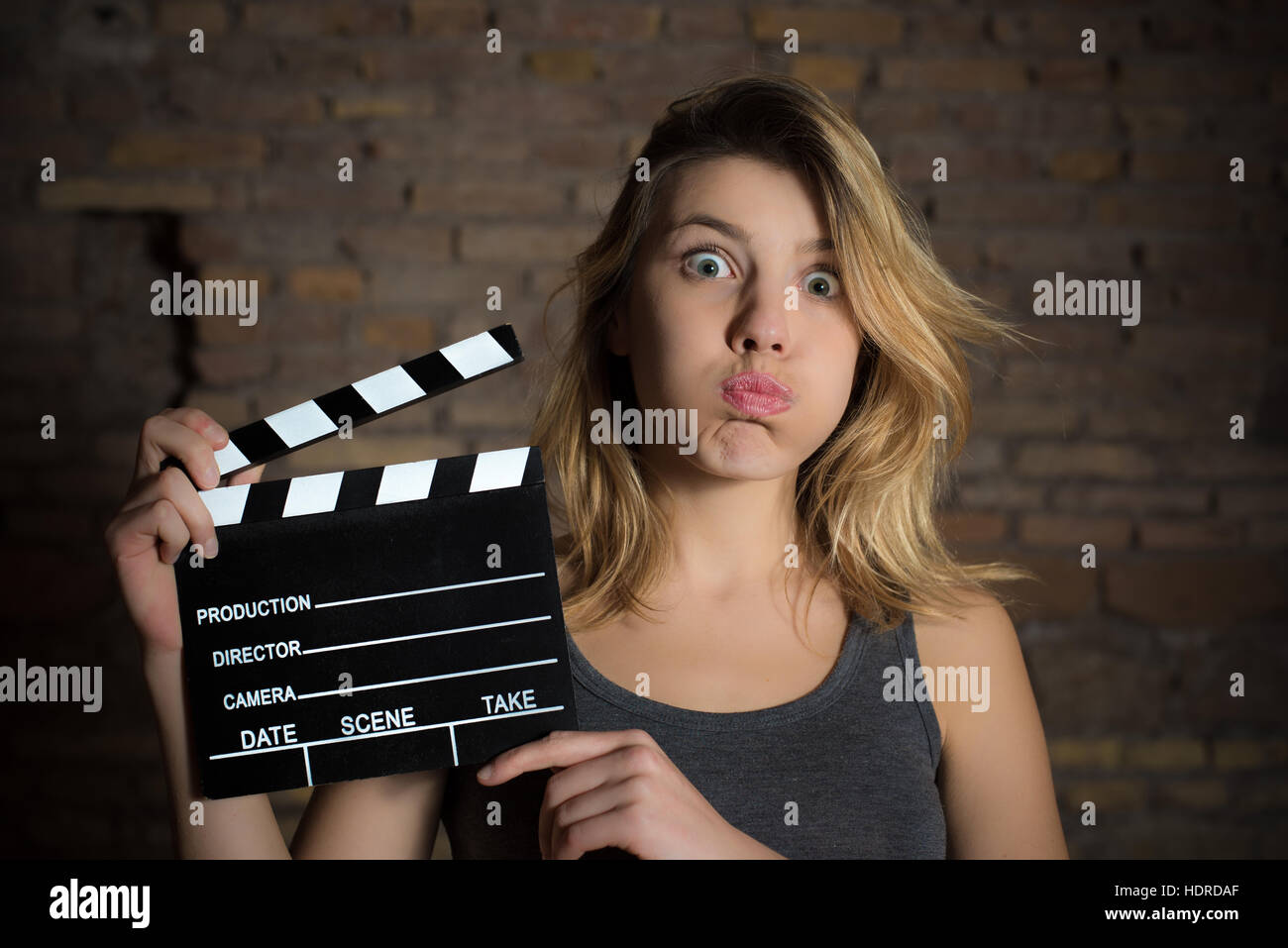 Young blonde girl grimace face and posing with movie clapper board for actress audition Stock Photo