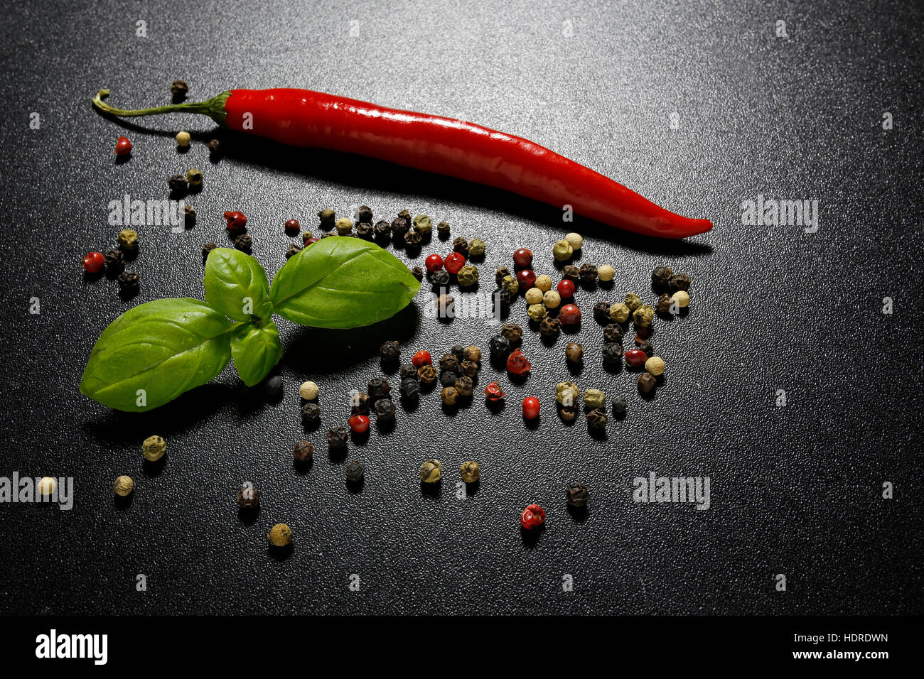 red chili pepper, basil leaves and mixed peppercorns on a shiny black