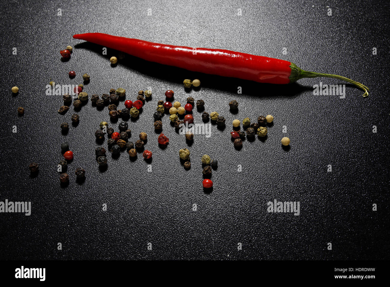 red chili pepper, basil leaves and mixed peppercorns on a shiny black