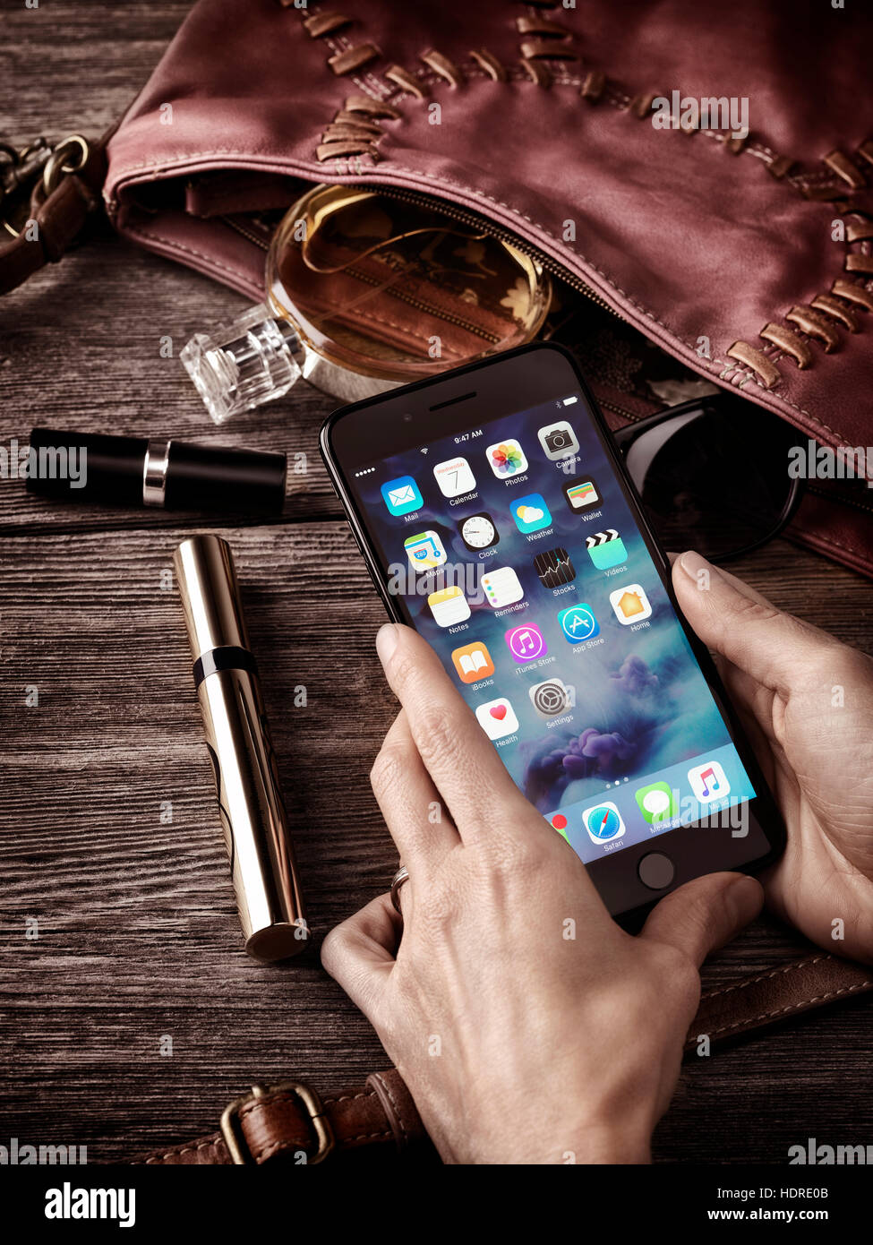 Woman hands holding Apple iPhone 7 Plus with her purse, makeup and accessories on the table conceptual still life Stock Photo