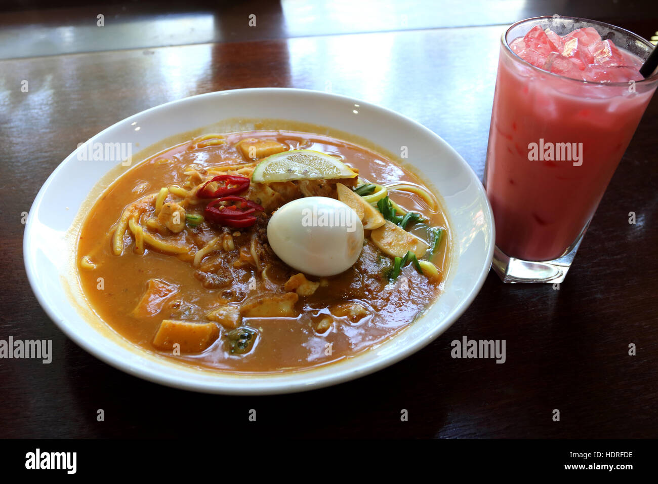 A bowl of Curry Laksa noodles, one of  Malaysians authentic dish with a glass of Milky Rose water syrup drink called Air Bandung Stock Photo
