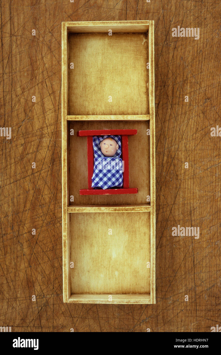 Small wooden tray with three compartments with middle one containing model of child or baby in bed Stock Photo