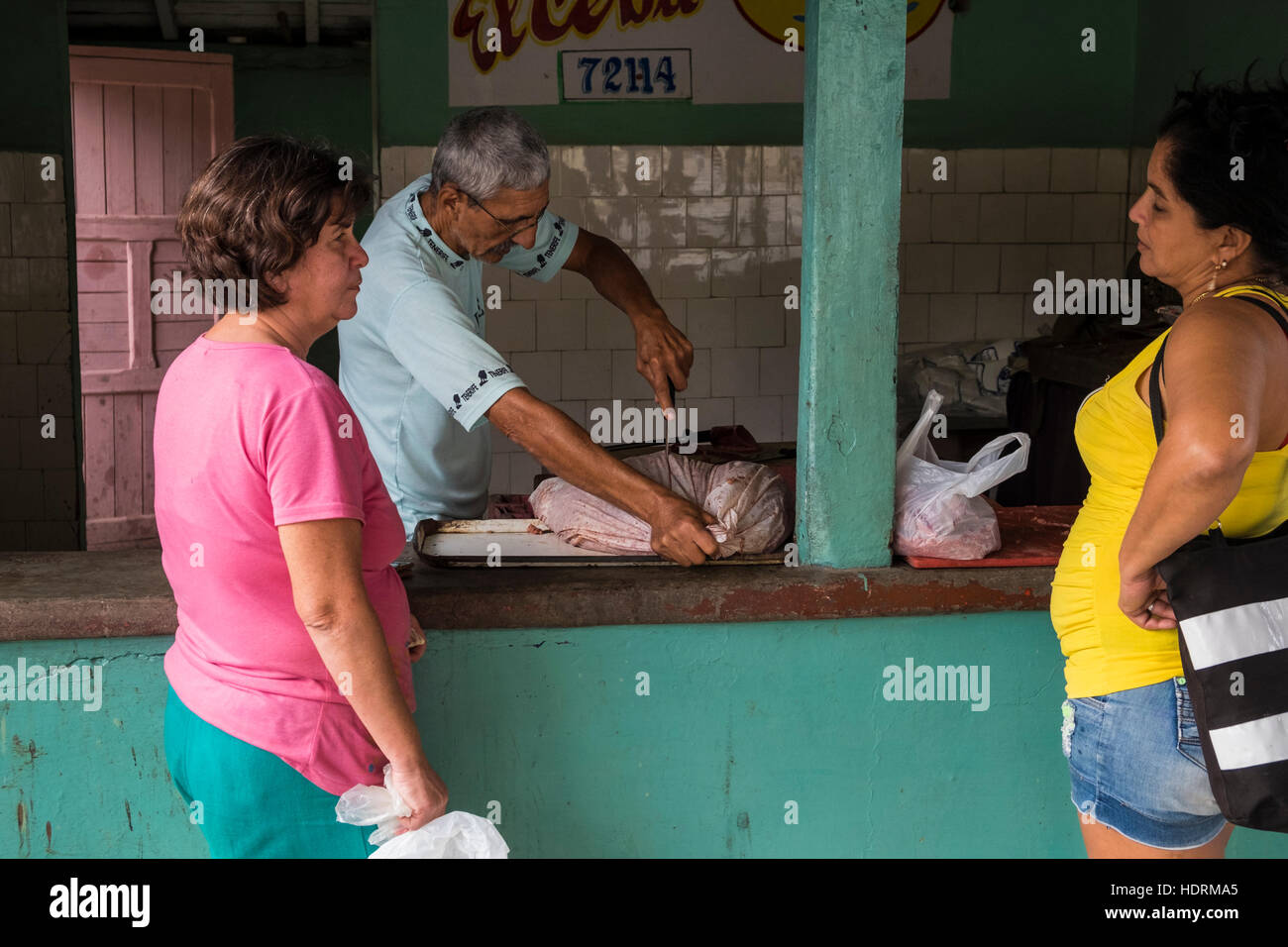 Women chatting while butcher opens bag of meat at ration shop in Vinales, Cuba Stock Photo
